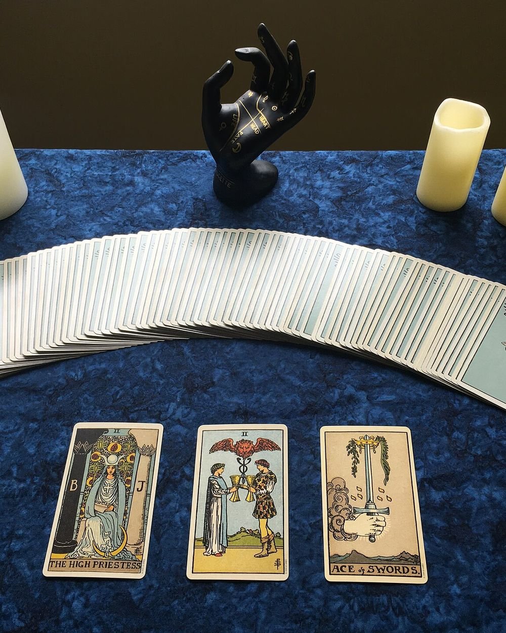 Tirage de trois cartes de tarot sur un tapis bleu nuit, entre deux bougies